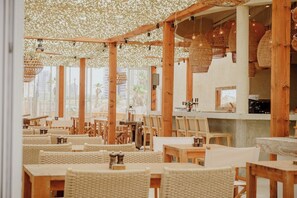 Een restaurant met houten meubels, geweven plafonddecoraties en grote ramen.