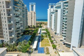 A high-rise residential building with a swimming pool, parking area, and a view of the beach. - Bright Beachside Oasis | Steps to the Shore (Netanya)