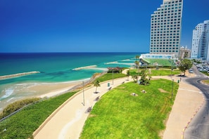A coastal hotel with a beach view, a parking area, and a pedestrian walkway. - Bright Beachside Oasis | Steps to the Shore (Netanya)
