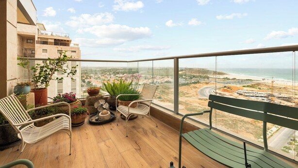 Un balcón con vista a la playa y al paisaje urbano, amueblado con sillas y plantas en macetas.