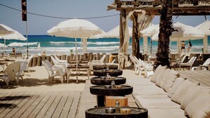 Un área de descanso frente a la playa con sillones, sombrillas, una terraza de madera y vistas al océano.