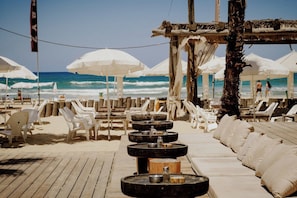 A beachside lounge area with lounge chairs and umbrellas, a wooden deck, and a view of the ocean. - Bright Beachside Oasis | Steps to the Shore (Netanya)