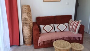 A room with a red sofa, two woven stools, a large woven basket, and a painting on the wall. - Gîte Terre d'ocre (Hérépian)