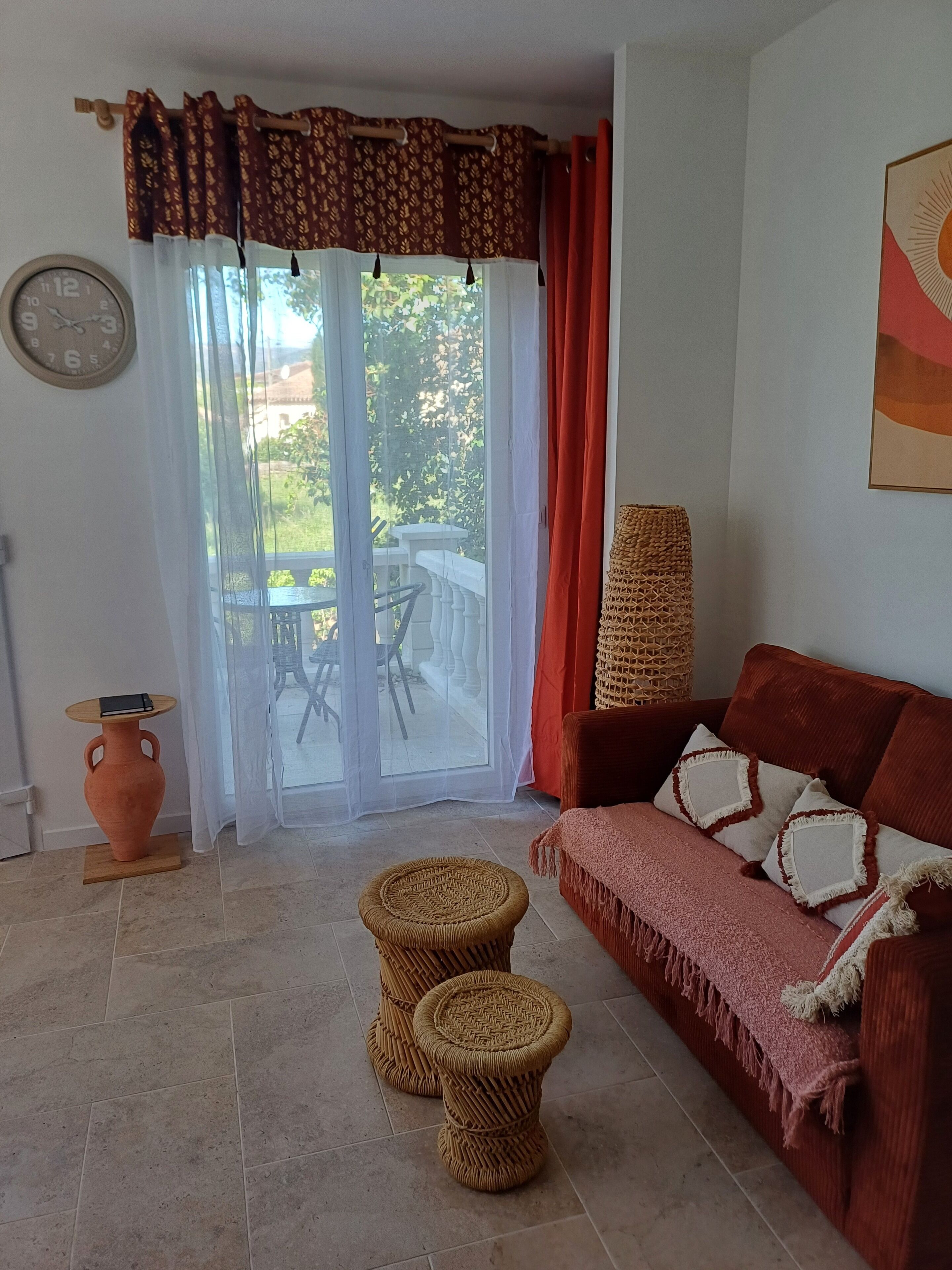 Un salon avec un canapé rouge, une table basse en osier, un vase en terre cuite et un tabouret en rotin.