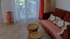 A living room with a red sofa, a woven coffee table, a terracotta vase, and a wicker stool. - Gîte Terre d'ocre (Hérépian)