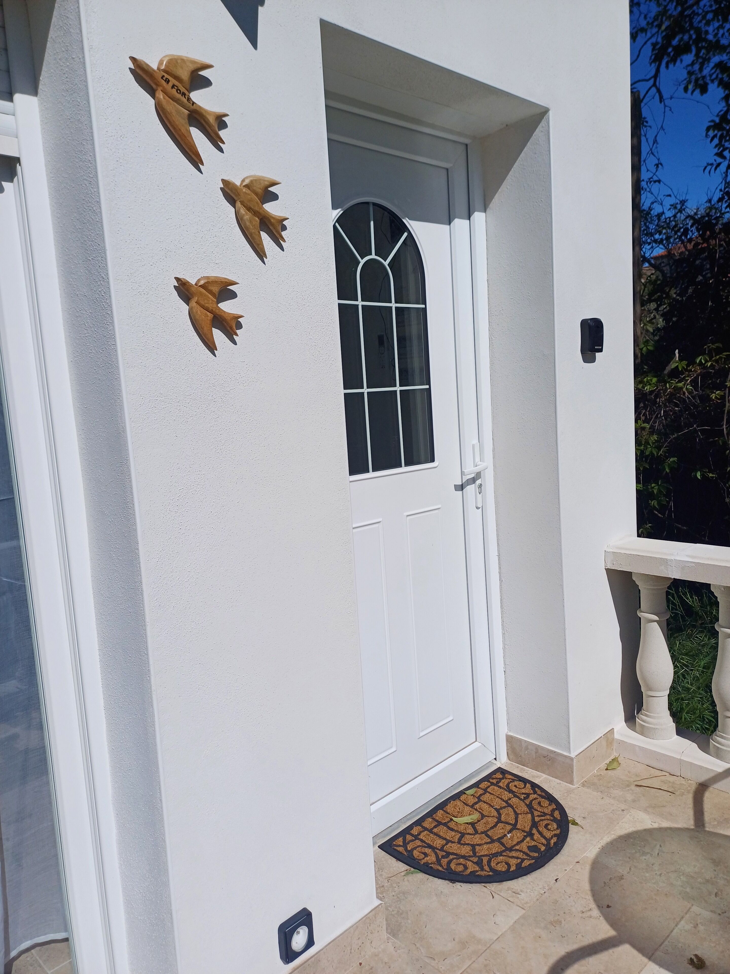 A white building with a white door, a window with a decorative grille, and three wooden animal figures on the wall.