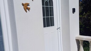 A white building with a white door, a window with a decorative grille, and three wooden animal figures on the wall. - Gîte Terre d'ocre (Hérépian)