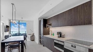 Eine moderne Küche mit dunklen Holzschränken, einer großen Kochinsel mit integriertem Backofen und Meerblick durch große Fenster.