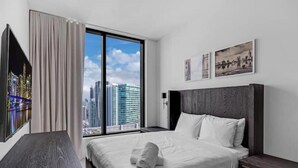 A hotel room with a large bed, a wooden nightstand, a desk, and a view of a cityscape through floor-to-ceiling windows. - SkyVilla Penthouse 3BD  3BA in Hotel 601 Miami (Miami)