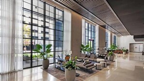Eine großzügige Lobby mit großen Fenstern, einer Sitzecke mit Sofas und einem Couchtisch sowie einigen Blumentöpfen.