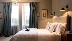 A neatly made bed with a quilted cover, a bedside table with a book, and two wall-mounted lamps. - Sleeps 18 in 5 king, 1 king with bunk, 1 twin and 1 bunk room (Kincraig)