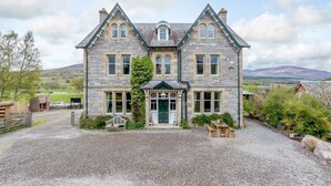 A stone building with a green door, multiple windows, and a gravel driveway. - Sleeps 18 in 5 king, 1 king with bunk, 1 twin and 1 bunk room (Kincraig)