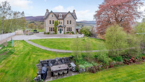 A large stone house with a well-maintained lawn and a stone patio with outdoor seating. - Sleeps 18 in 5 king, 1 king with bunk, 1 twin and 1 bunk room (Kincraig)