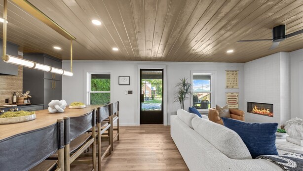 Una sala moderna con chimenea, un comedor con mesa y bancos de madera, y una cocina con horno empotrado.