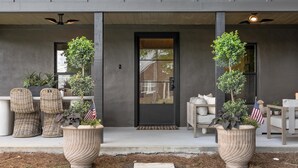 Entrada moderna de un edificio con puerta oscura, plantas en macetas, cestas de mimbre y asientos al aire libre.