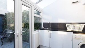 Eine kleine Küche mit Waschmaschine, Spüle und Fenster mit Blick auf einen Garten.