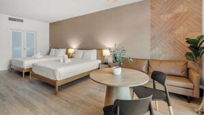 Quarto de hotel com duas camas de solteiro, uma mesa de jantar redonda com cadeiras, um sofá e uma planta em vaso.