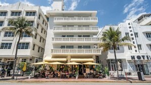 Um hotel com vários andares, mesas ao ar livre e palmeiras.