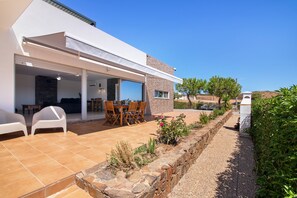 A modern house with a patio, a dining area, and a stone retaining wall.