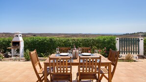 Une terrasse avec une table dressée pour quatre personnes, un barbecue et une vue sur la campagne.