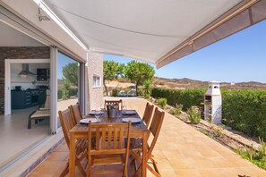 An outdoor dining area with a table and chairs, a pergola, and a view of the landscape.