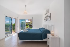 A bedroom with a bed, a nightstand, a lamp, and a view of the outdoors through a sliding door.
