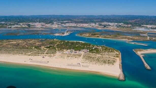 Une vue aérienne d’une zone côtière avec une plage, un port de plaisance et une ville en arrière-plan.