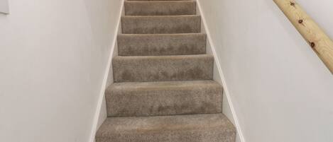 Un escalier recouvert de moquette, doté de rampes en bois, menant à l’étage supérieur.