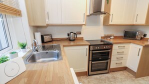 A modern kitchen with a stainless steel sink, a toaster, an oven, and wooden cabinets. - Lonsdale Street (Workington)