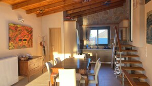 Ein Essbereich mit Holztisch und Stühlen, eine Küche mit Steinwand sowie eine Treppe.