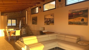 Ein geräumiger Wohnbereich mit einer großen, weißen L-förmigen Couch, einem Esstisch mit Stühlen, einer Küchenzeile und einer Treppe, die zu einer oberen Ebene führt.