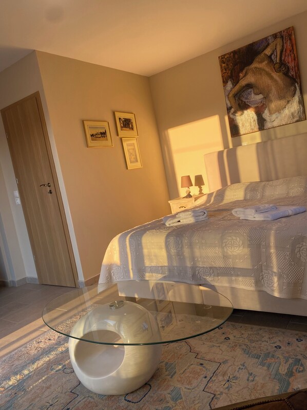 Un dormitorio con una cama, una mesa de vidrio, un tapete estampado y cuadros en la pared.