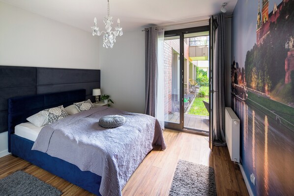 A bedroom with a large bed, a chandelier, and a view of a garden through a sliding door.