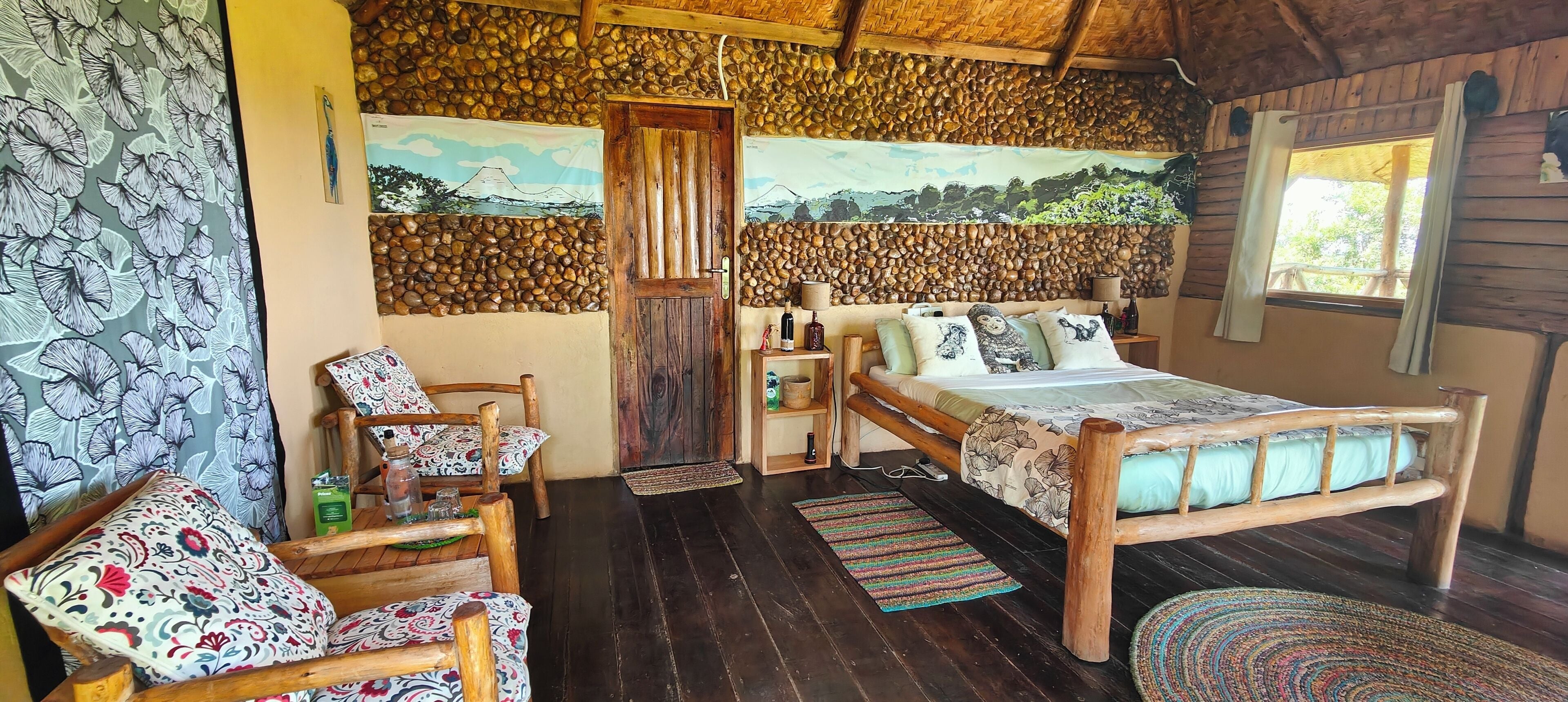 A room with a bed, wooden chairs, a small table, and a wall with a stone pattern.