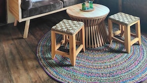 Ein rustikaler Raum mit einem Strohdach, einer Couch mit Kissen, einem runden Holztisch und einem gewebten Teppich.