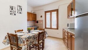 Un coin repas avec une table dressée pour quatre personnes, des chaises en bois et une cuisine dotée de meubles en bois et d’un réfrigérateur.