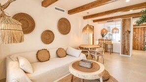 Un salon moderne comprenant un canapé, des éléments de décoration murale ronds en fibres tressées, une table basse ronde en bois et un coin repas avec une table et des chaises en bois.