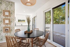 A dining area with a round table, wicker chairs, a vase, and a view through large sliding doors to an outdoor patio. - Holiday Home 'Vinha' with Private Terrace, Private Garden and Wi-Fi (Óbidos)