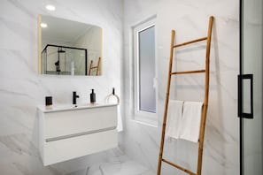 A bathroom with a white marble wall, a mirror, a vanity with a black faucet, and a wooden ladder leaning against the wall.