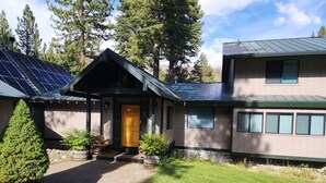 Ett tvåvåningshus med ett grönt tak, solpaneler och en veranda framför huset med krukväxter.