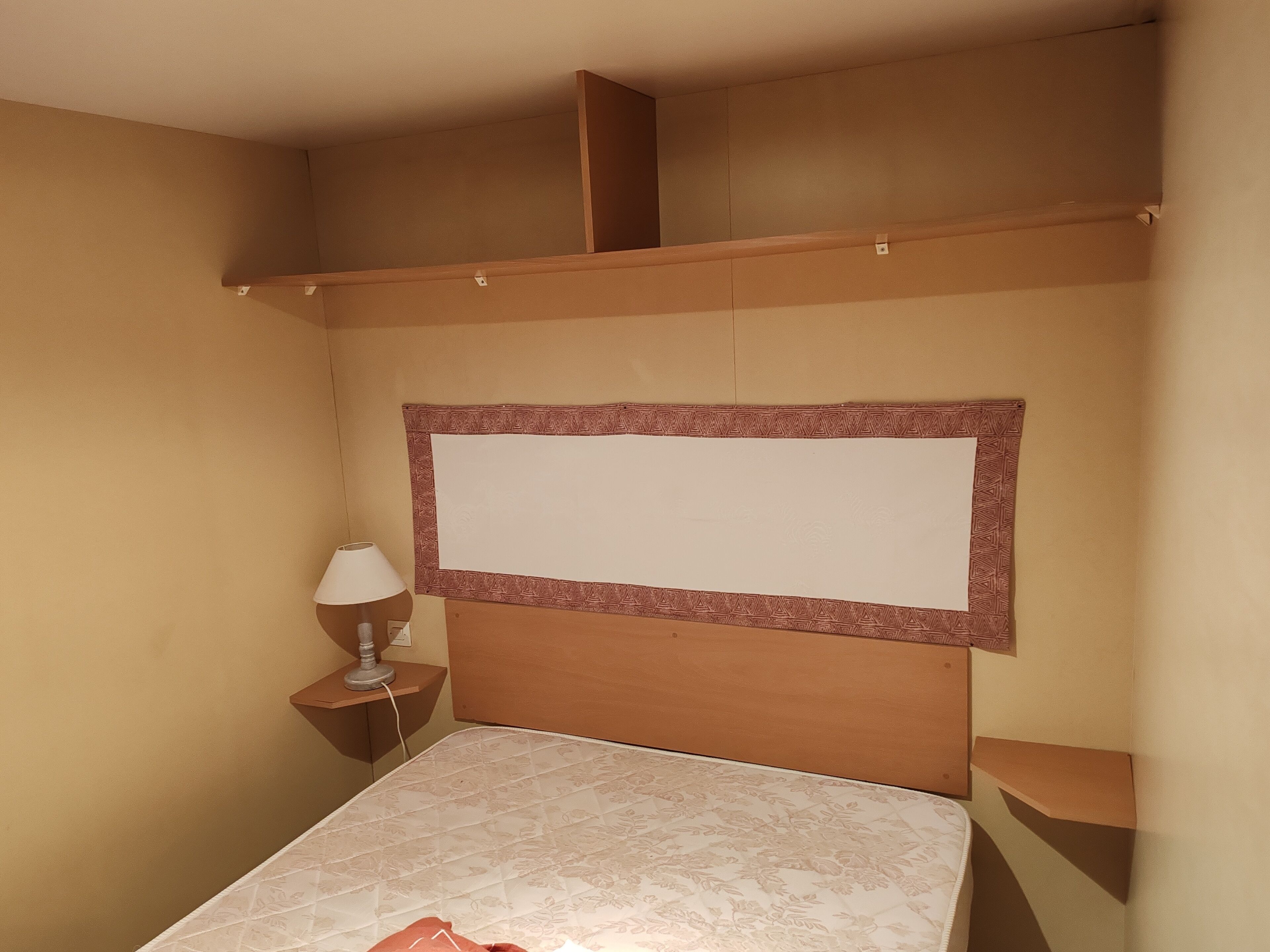 A bedroom with a bed, a nightstand, a lamp, and a bulletin board.