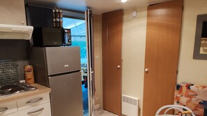 Cozinha compacta com geladeira, fogão e micro-ondas. Há uma mesa pequena com uma cesta e uma cadeira.