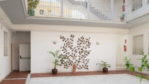 A spacious courtyard with a white tiled floor, potted plants, a decorative wall art, and a staircase leading to an upper level. - Modern Studio by the River with Wi-Fi and Air Conditioning (Seville)