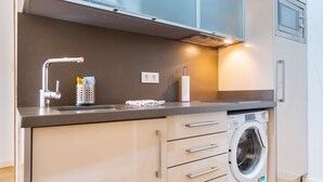 A compact kitchen with a built-in washing machine, a modern faucet, and a small countertop. - Modern Studio by the River with Wi-Fi and Air Conditioning (Seville)
