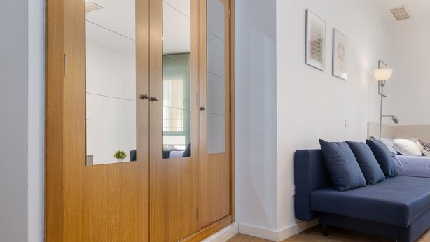 A bedroom with a wooden wardrobe, a blue sofa, and a bedside table. - Modern Studio by the River with Wi-Fi and Air Conditioning (Seville)