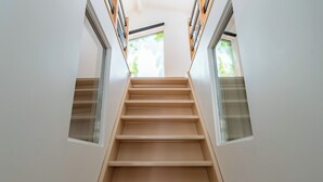 Eine modern gestaltete Treppe, gesäumt von Glaspaneelen und Holzelementen, führt in einen hellen Bereich mit natürlichem Licht.