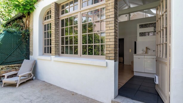 Ein Zimmer mit großem Fenster, einem kleinen Balkon mit Stuhl und sichtbarer Küchenzeile.