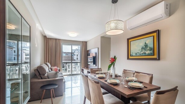 Uma área de refeições moderna com uma mesa de madeira posta para quatro pessoas, um sofá e uma grande janela com vista para a paisagem urbana.