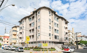 Un immeuble à plusieurs étages doté de balcons, un passage piéton et une rue bordée de voitures garées.