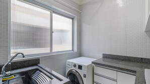 Ett tvättrum med tvättmaskin, handfat och ett fönster med persienner.